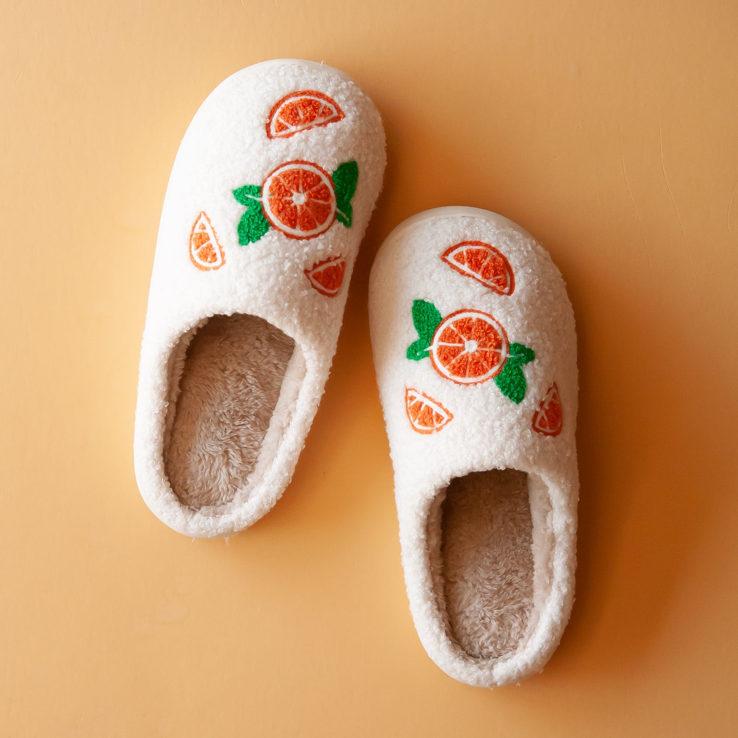 Pair of cozy slippers with custom designed oranges on each slipper, featuring a soft, plush exterior and a fluffy interior lining for maximum comfor