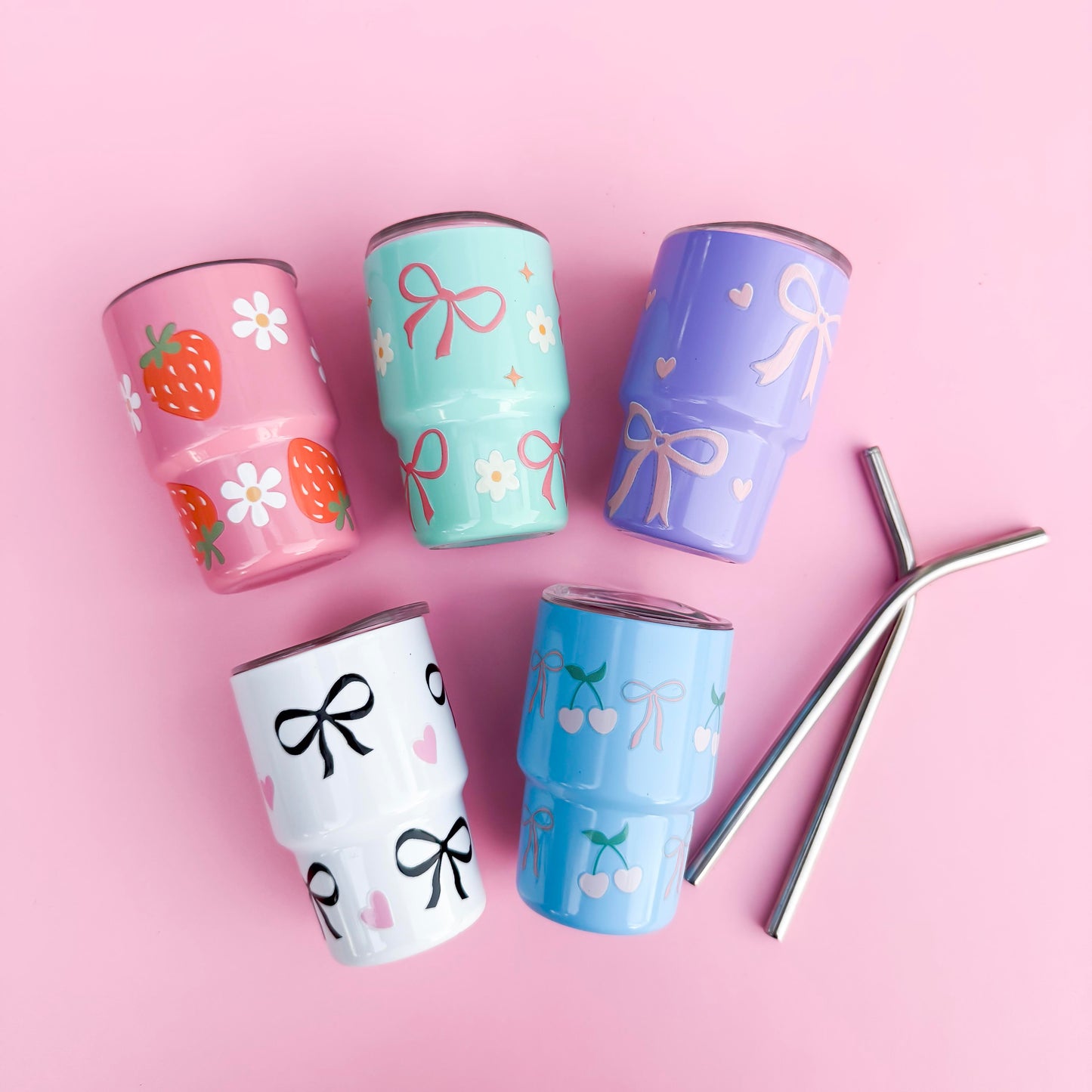 Set of 5 mini 3oz stainless steel tumblers with reusable metal straws, featuring hand-painted pastel designs of bows, hearts, cherries, strawberries, and florals on a pink background