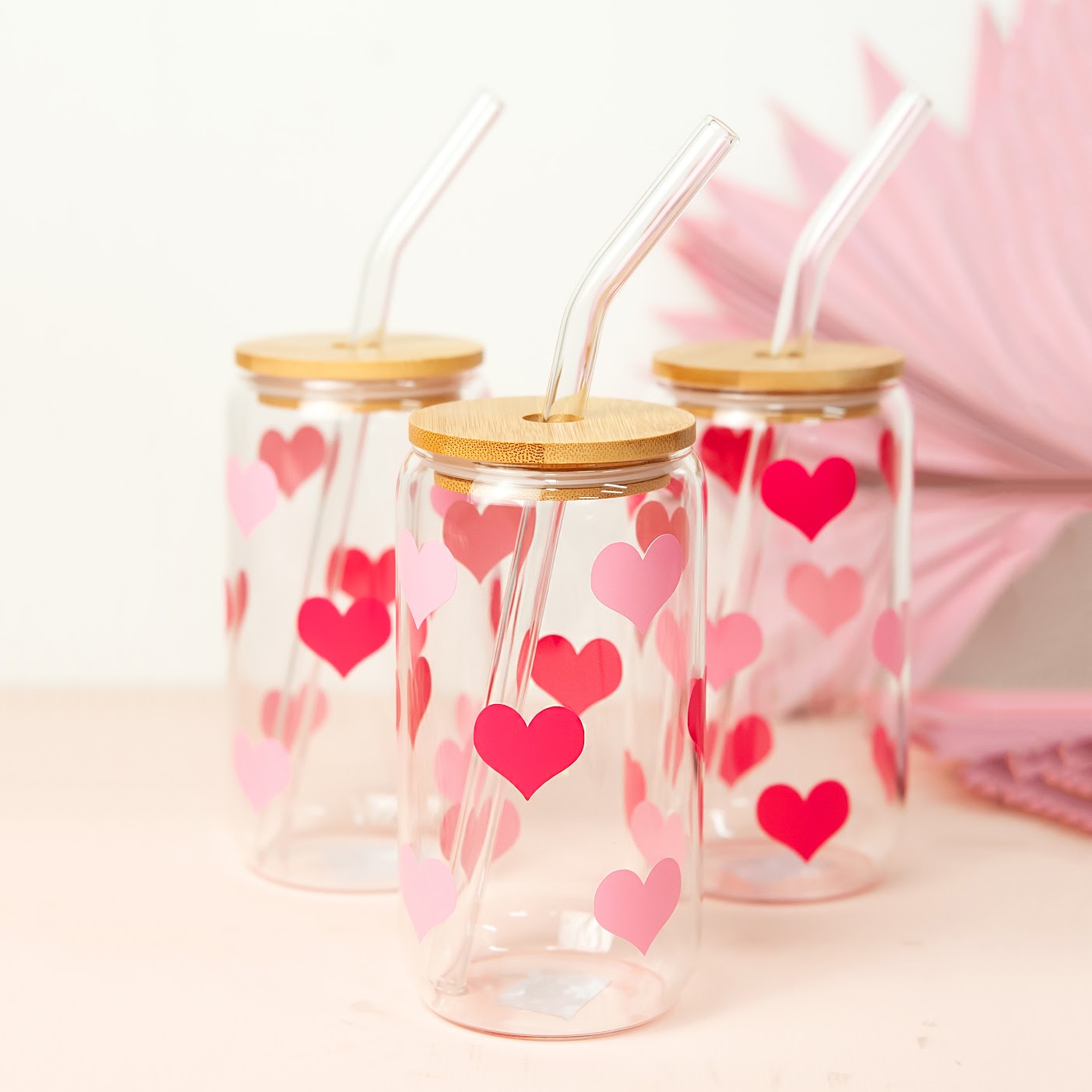 Adorable glass tumbler decorated with pink and red heart designs, featuring a bamboo lid and glass straw, ideal for Valentine's Day or everyday use