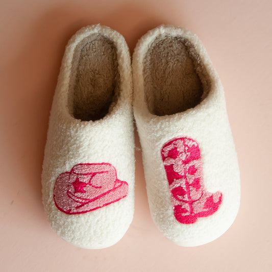 Cozy white slippers featuring embroidered designs of a pink cowboy hat and boot, perfect for warm and stylish indoor wear.