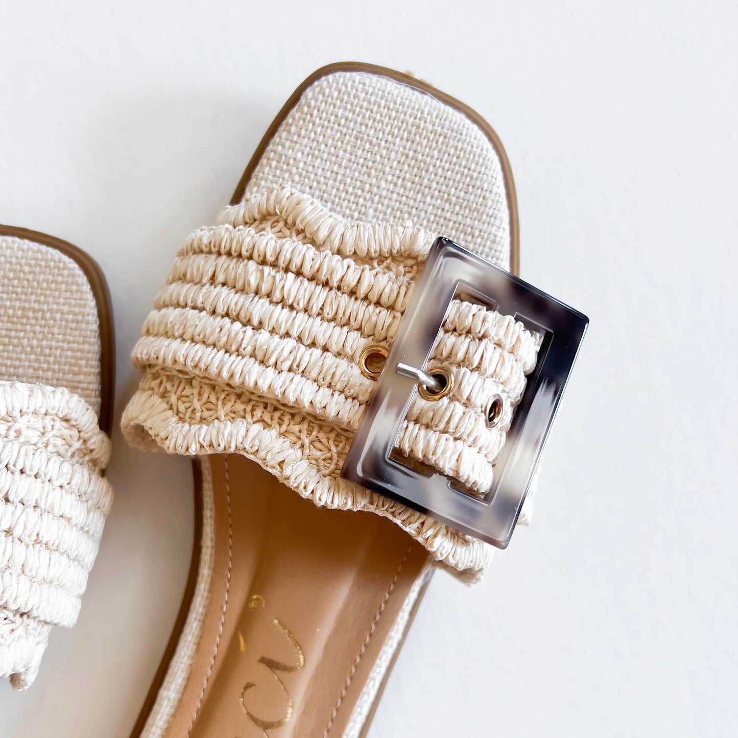 Leslie Sandal with textured strap and oversized buckle on white background with green palm leaves