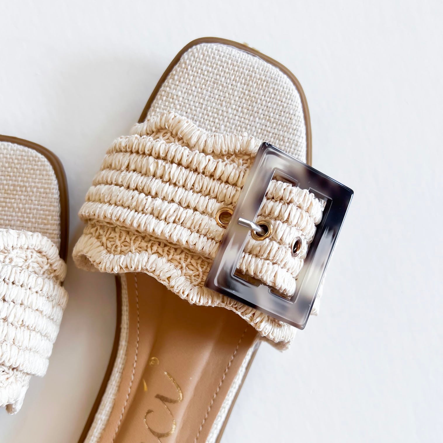 Leslie Sandal with textured strap and oversized buckle on white background with green palm leaves