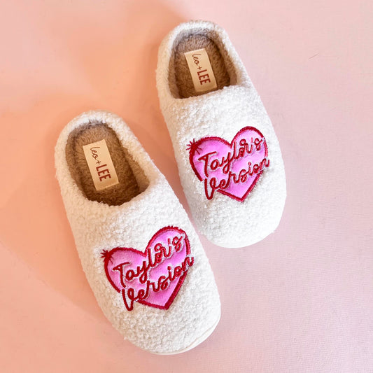 Pair of cozy slippers from Taylor's Version collection, featuring a soft, plush exterior in a light beige color with embroidered detailing and a fluffy interior lining for maximum comfort