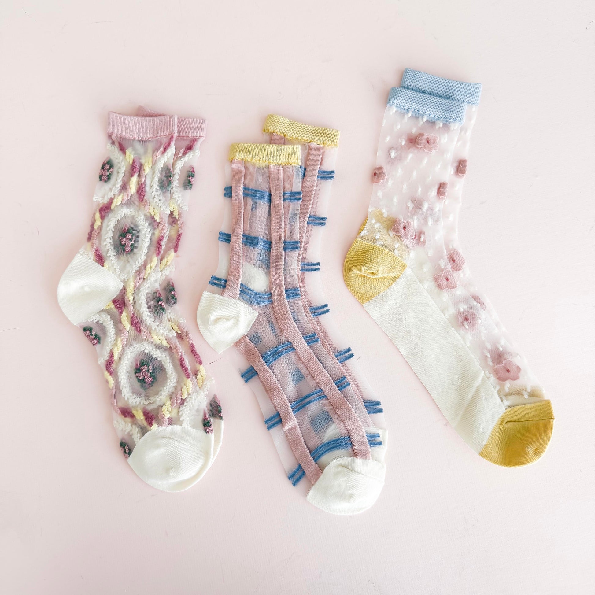 Set of three sheer embroidered pastel socks featuring floral, grid, and bear designs, perfect for stylish and whimsical looks